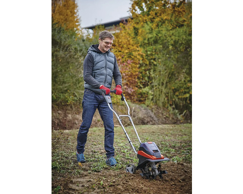 Ein Mann benutzt eine Motorhacke im Garten, um den Boden zu bearbeiten.