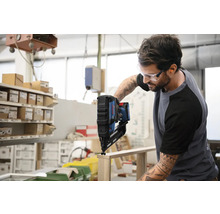 Ein Mann verwendet einen Akku-Nagler von Bosch auf einem Holzstück.