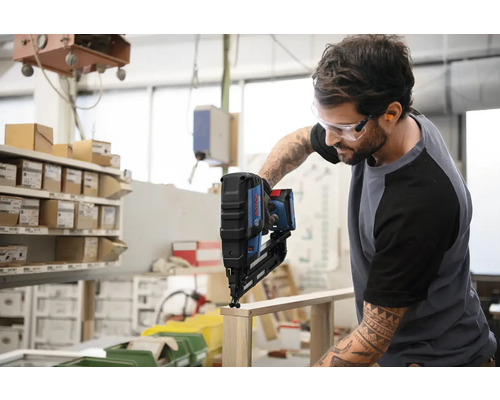 Ein Mann verwendet einen Akku-Nagler von Bosch auf einem Holzstück.