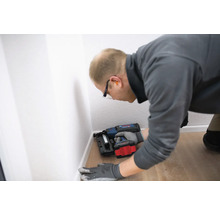 Handwerker befestigt Fußleisten mit einem Akku-Nagler an einer Wand.