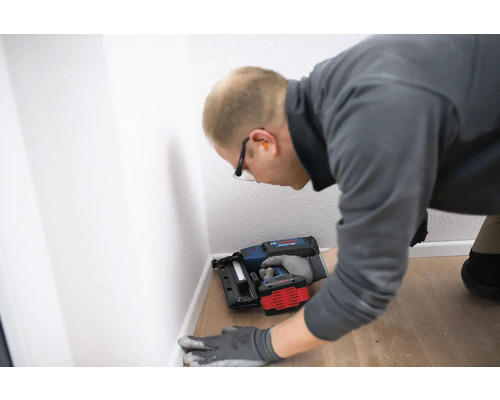 Handwerker befestigt Fußleisten mit einem Akku-Nagler an einer Wand.