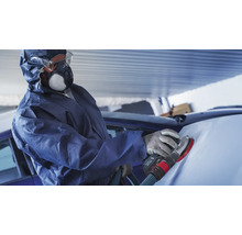 Person im Schutzanzug schleift ein Auto mit einem Schleifgerät.