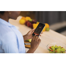 Frau bedient ein Smartphone mit Temperaturanzeige in der Küche