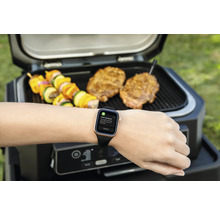 Grill mit Grillgut und Smartwatch am Handgelenk