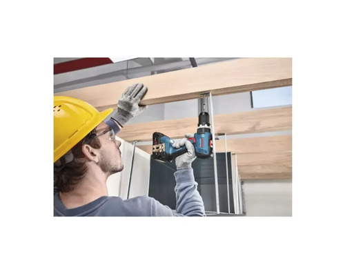 Handwerker mit Schutzhelm bohrt mit einem Akkubohrer ein Holzbrett an einer Deckenkonstruktion.