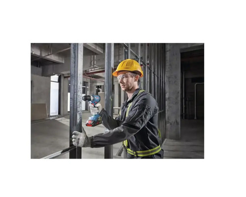 Ein Mann mit Schutzhelm und Schutzbrille benutzt einen Akkuschrauber in einem Rohbau.