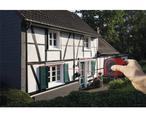 Eine Person verwendet ein Laser-Messgerät an einem Haus, um eine horizontale Linie anzuzeigen.