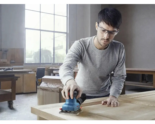 Ein Mann schleift Holz mit einem Schwingschleifer in einer Werkstatt.