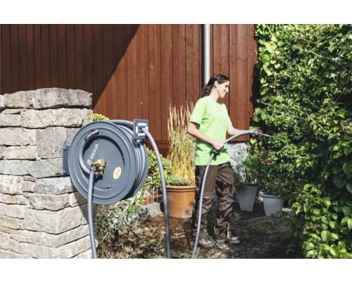 Frau bewässert Pflanzen mit einer Geka Gartenschlauchbox im Garten.