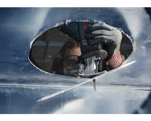 Nahaufnahme einer Person mit Schutzbrille, die mit einer Stichsäge ein Loch in eine Metallplatte schneidet.