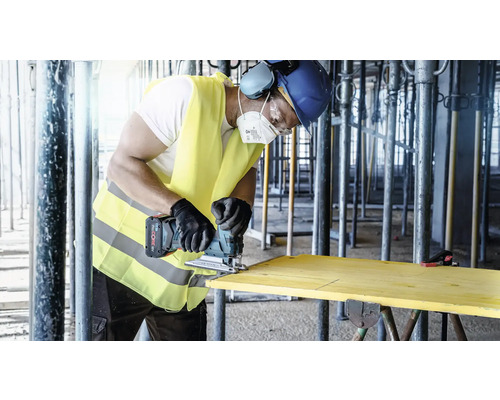 Handwerker sägt Holzbrett mit einer Akku-Stichsäge auf einer Baustelle.