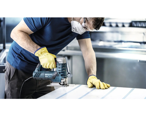 Handwerker mit Schutzmaske, Schutzbrille und Handschuhen sägt mit einer Stichsäge ein Werkstück.