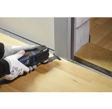 Eine Person verwendet ein Multifunktionswerkzeug, um eine Türzarge auf einem Holzboden zu bearbeiten.