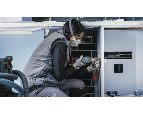 Eine Handwerkerin arbeitet mit einem Multifunktionswerkzeug an einem Waschtisch im Badezimmer.