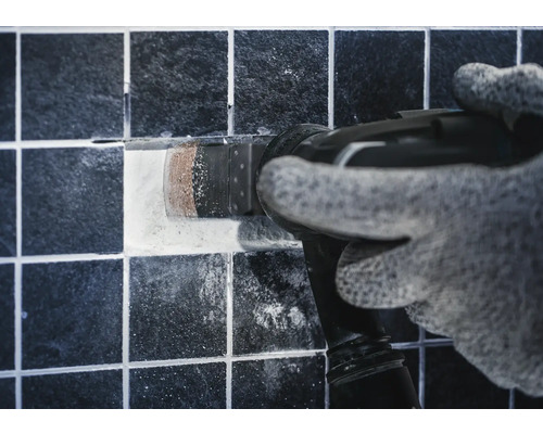 Handwerker mit Multifunktionswerkzeug entfernt eine Fliese.