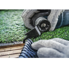 Nahaufnahme einer Hand mit Handschuh, die mit einem Multifunktionswerkzeug Kunstrasen schneidet.