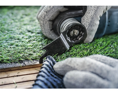 Nahaufnahme einer Hand mit Handschuh, die mit einem Multifunktionswerkzeug Kunstrasen schneidet.