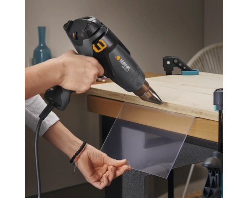 Handwerker verwendet Heißluftpistole zum Erhitzen einer Kunststoffplatte auf einer Werkbank.