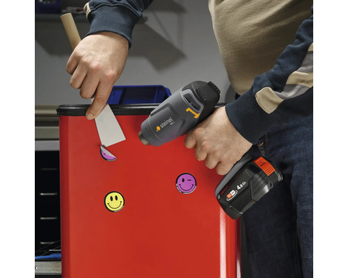 Eine Person entfernt mit einem Spachtel und einer Heißluftpistole Aufkleber von einem roten Behälter.