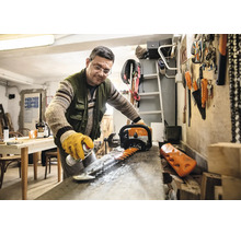 Ein Mann reinigt die Klinge einer Heckenschere mit einem Spray in einer Werkstatt.