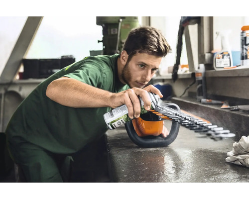 Mann sprüht Pflegespray auf eine Heckenschere, um die Klingen zu warten.