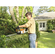 Eine Frau schneidet eine Hecke mit einer Heckenschere von Stihl im Garten.