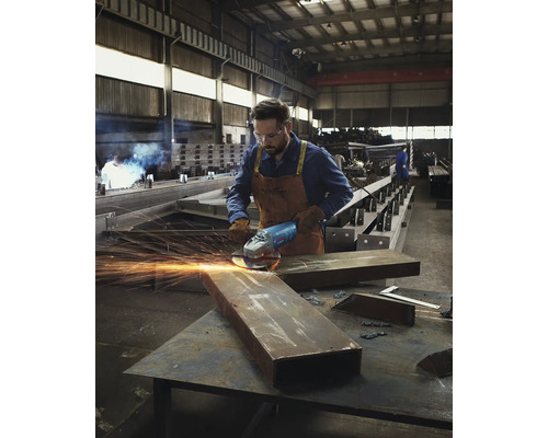 Mann schleift Metall mit einem Winkelschleifer in einer Werkstatt.