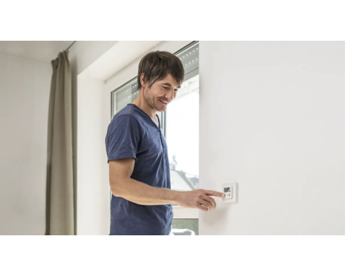 Mann bedient einen digitalen Thermostat an einer Wand zur Temperaturregelung.