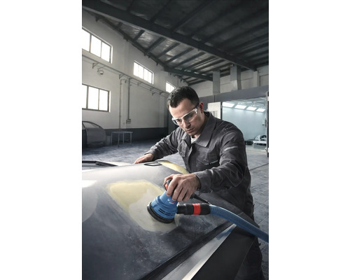 Ein Mann schleift eine Motorhaube mit einem Exzenterschleifer in einer Werkstatt.