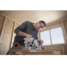 Ein Mann sägt mit einer Bosch Kreissäge ein Holzbrett in einem Rohbau.