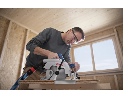 Ein Mann sägt mit einer Bosch Kreissäge ein Holzbrett in einem Rohbau.