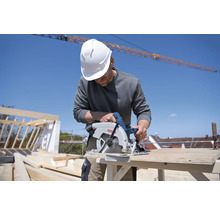 Handwerker mit Schutzhelm sägt Holz mit einer Bosch Kreissäge auf einer Baustelle.