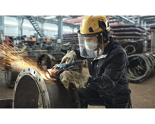 Ein Arbeiter schleift mit einer Flex ein Metallrohr, wobei Funken sprühen.