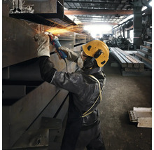 Ein Arbeiter schleift Metall mit einem Winkelschleifer in einer Werkshalle, während Funken sprühen.