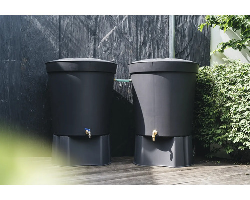 Zwei dunkle Regentonnen aus Kunststoff mit Sockel und Wasserhahn vor einer dunklen Wand