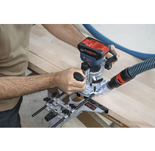 Eine Oberfräse wird zum Bearbeiten eines Holzstücks verwendet. Ein Staubsaugerschlauch ist an der Maschine befestigt.