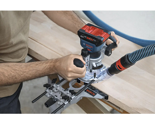 Eine Oberfräse wird zum Bearbeiten eines Holzstücks verwendet. Ein Staubsaugerschlauch ist an der Maschine befestigt.