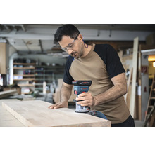 Ein Mann verwendet eine Bosch Oberfräse an einem Holzbrett in einer Werkstatt.