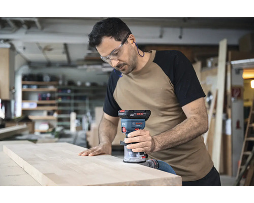 Ein Mann verwendet eine Bosch Oberfräse an einem Holzbrett in einer Werkstatt.