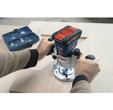 Eine Person benutzt eine Bosch Akku Oberfräse auf einem Holzbrett, mit einem blauen Werkzeugkasten im Hintergrund.