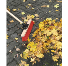 Kehrbesen mit Holzstiel und Herbstlaub auf Pflastersteinen