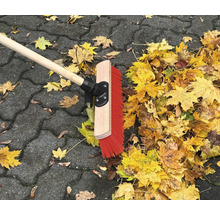 Straßenbesen mit Holzstiel und Herbstlaub auf Pflastersteinen