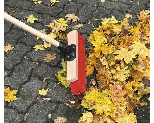 Straßenbesen mit Holzstiel und Herbstlaub auf Pflastersteinen