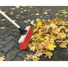 Besen kehrt Herbstlaub auf Pflastersteinen zusammen