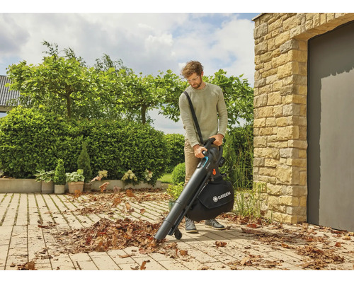 Ein Mann benutzt einen Laubsauger von Gardena auf einer gepflasterten Fläche, um Laub zu entfernen.