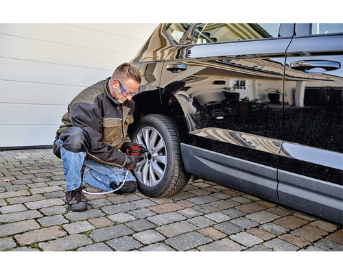 Mann wechselt mit einem Druckluft-Schlagschrauber einen Reifen an einem schwarzen Auto