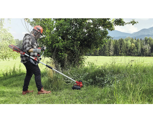 Eine Person, die einen Akku-Rasentrimmer in einem grasbewachsenen Außenbereich bedient.