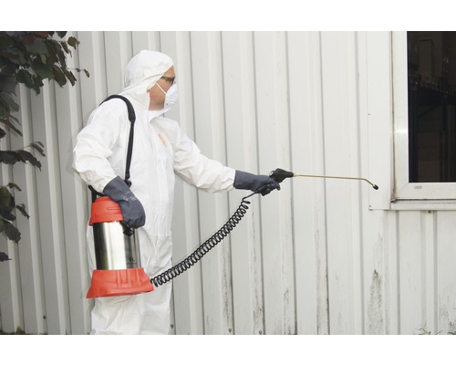 Person im Schutzanzug sprüht Fassade mit Sprühgerät