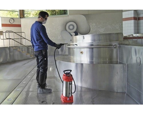 Eine Person reinigt einen Poolbereich mit einem Drucksprüher. Der Sprüher steht auf dem Boden.