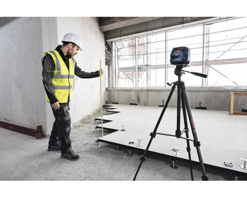 Handwerker mit Laser-Wasserwaage und Nivellierlatte bei der Installation eines Doppelbodens.